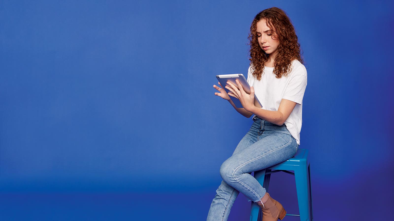 Teenage girl sitting on a stool using a tablet.